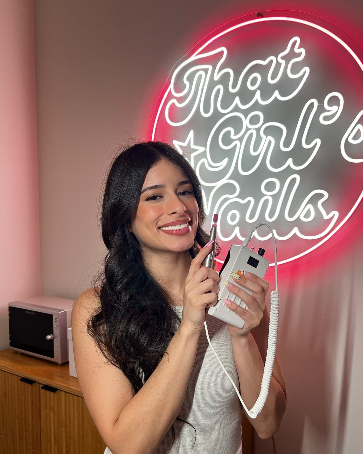 Andrea, licensed nail technician and owner of That Girl's Nails, holding an e-file in front of the salon's neon sign